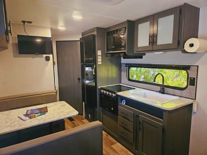 RV rental: modern kitchen with dark cabinets, white counters & sink, plus a cozy dinette & TV, ready for travel.. Dutchmen TT 2024