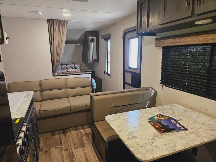 Explore the comfortable interior of this RV rental, featuring a practical dinette, plush sofa, and compact kitchen area.. Dutchmen TT 2024