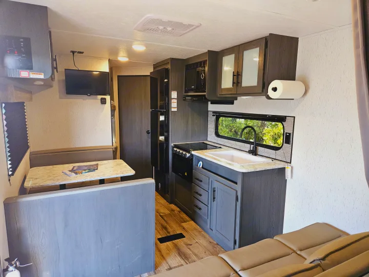 Bright RV rental interior featuring a kitchen with a sink & stove, dinette, TV, and comfortable sofa seating.. Dutchmen TT 2024