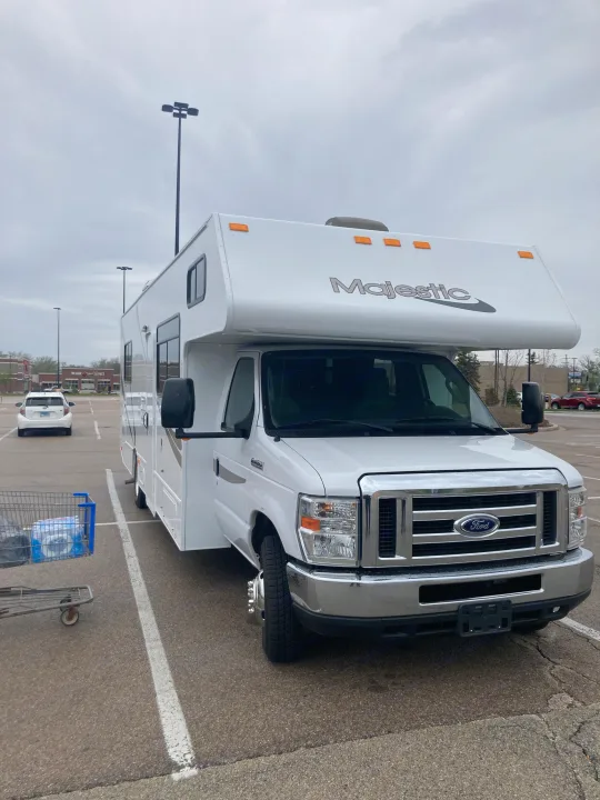 White Ford Majestic RV rental parked in a grocery store lot on an overcast day, with a shopping cart in the foreground.. Thor Majestic 2019