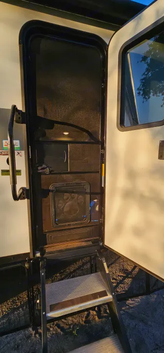 RV rental entry: open screen door with pet door, grab handle, & extended steps ready for travelers.. Forest River Wildwood X-Lite Platinum 2024