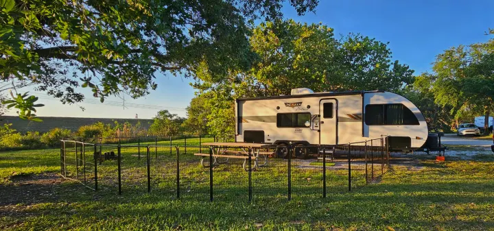 This RV rental campsite features a white travel trailer, a black pet fence, and a picnic table, perfect for outdoor camping.. Forest River Wildwood X-Lite Platinum 2024
