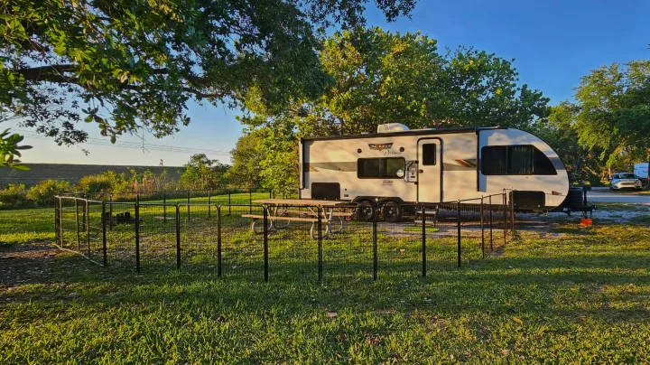 This rv rental is set up in a spacious campsite with a pet enclosure, picnic table, and natural surroundings.. Forest River Wildwood X-Lite Platinum 2024
