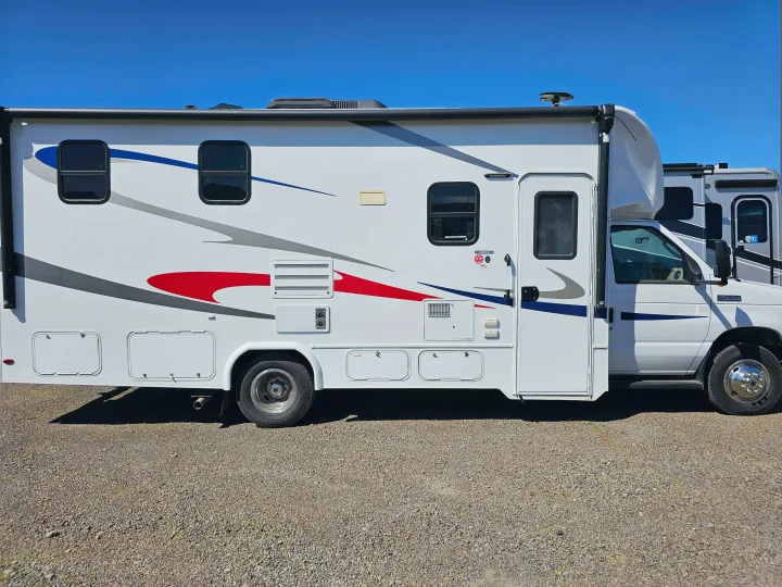 White Class C rv rental with colorful red, blue, and gray decals, parked on gravel under a clear blue sky.. Forester 2421MS 2019