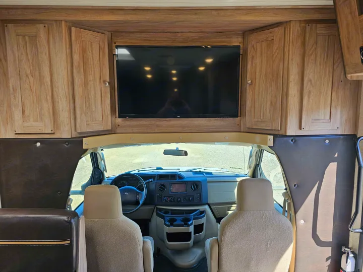 View of an RV rental's inviting interior: mounted TV, overhead wood cabinets, and the front driving area.. Forester 2421MS 2019