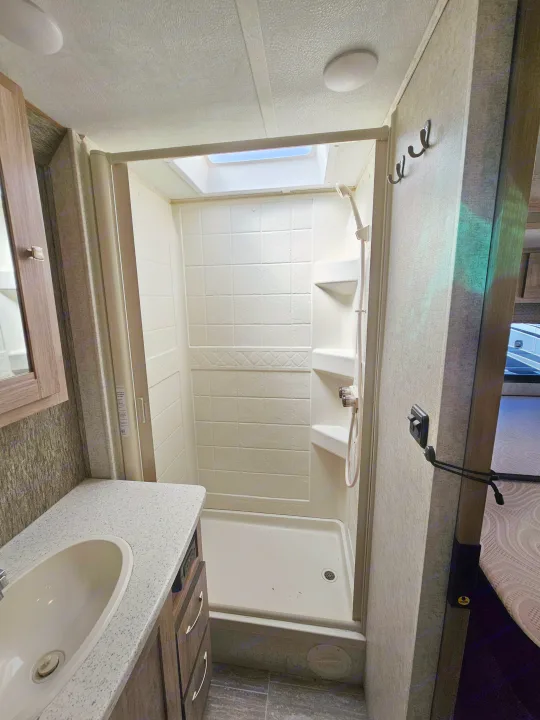 Inside an RV rental: a compact yet functional bathroom featuring a bright shower with skylight, vanity sink, and storage hooks.. Forester 2421MS 2019