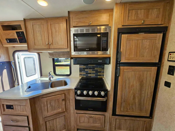 Bright rv rental kitchen: wood cabinets, microwave, stove, oven, fridge, and sink with tiled backsplash.. Forester 2421MS 2019