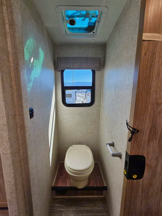 Compact RV rental bathroom with toilet, window, and ceiling vent, showing space-saving design.. Forester 2421MS 2019