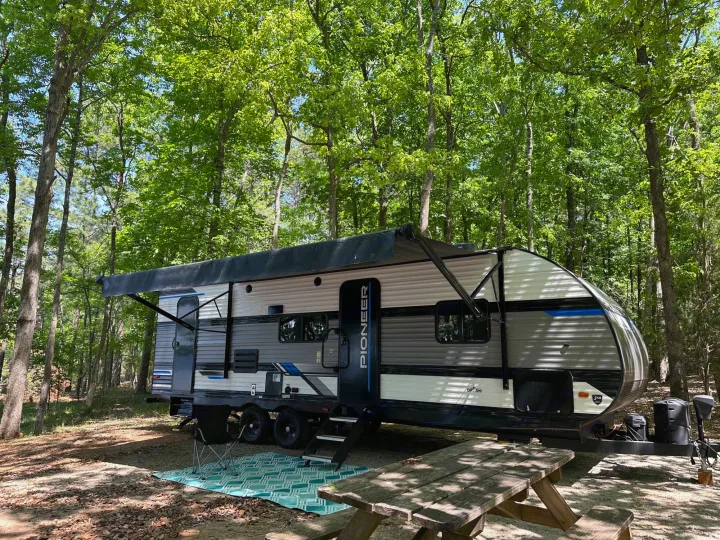 RV rental parked at a peaceful, shaded campsite with a picnic table and extended awning.. Heartland Pioneer BH270 2023