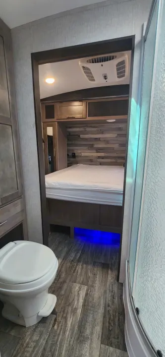 RV rental interior: Modern bedroom with blue under-bed lighting, AC, and storage, adjacent to bathroom (toilet/shower).. Crossroads Sunset Trail 2022