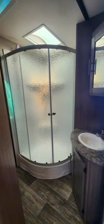 Inside this RV rental, find a well-appointed bathroom featuring a curved frosted glass shower, sink vanity, and mirrored cabinet.. Crossroads Sunset Trail 2022
