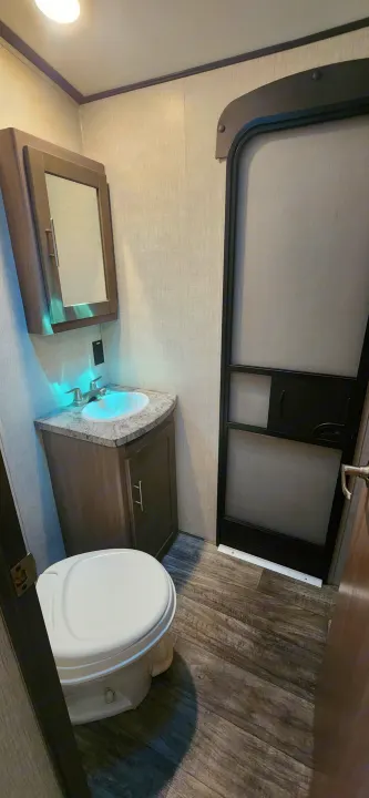 Compact RV rental bathroom featuring toilet, sink with blue LED lighting, vanity, mirror cabinet, and wood-look floor.. Crossroads Sunset Trail 2022