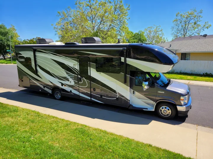 A sleek Esteem Class C rv rental with bold black and white graphics is parked on a sunny street, ready for journeys.. Entegra Coach Esteem 2021