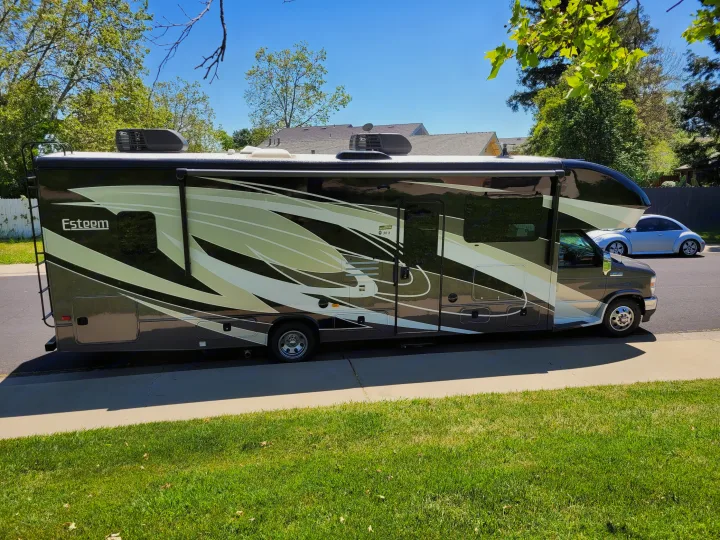 Side view of a large, modern Esteem RV rental in black, white, and green graphics, parked on a sunny day.. Entegra Coach Esteem 2021