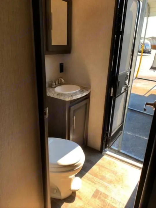 Compact RV rental bathroom featuring a toilet, sink, and mirror. An open door reveals the exterior.. Crossroads Sunset Trail 2021