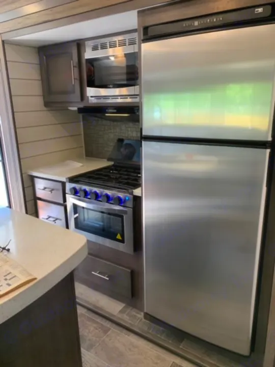 RV rental kitchen with stainless steel refrigerator, gas range, microwave, and modern cabinetry. Compact design.. Crossroads Sunset Trail 2021