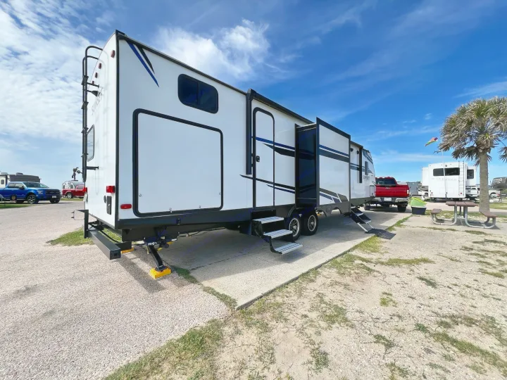 This white travel trailer RV rental, with extended slide-outs, is set up for camping at a sunny RV park.. Crossroads Sunset Trail 2021