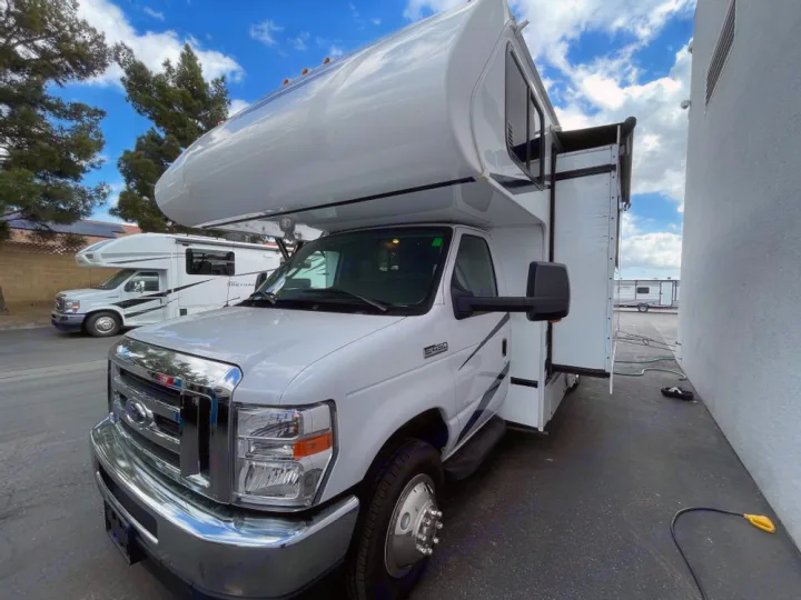 Two white Class C motorhomes, ready for rv rental, parked on a lot. The front RV has an extended slide-out.. Gulf Stream Conquest 2023