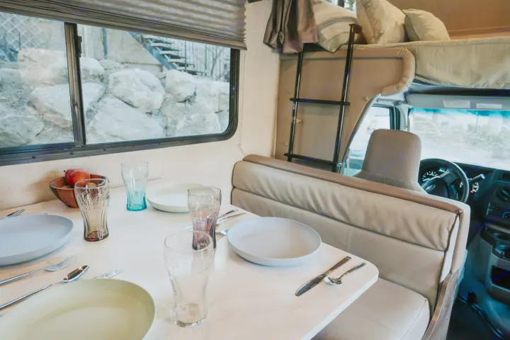 Spacious RV rental interior featuring a set dining table, a cozy overhead bed, and a view of nature outside.. Gulf Stream Conquest 2023