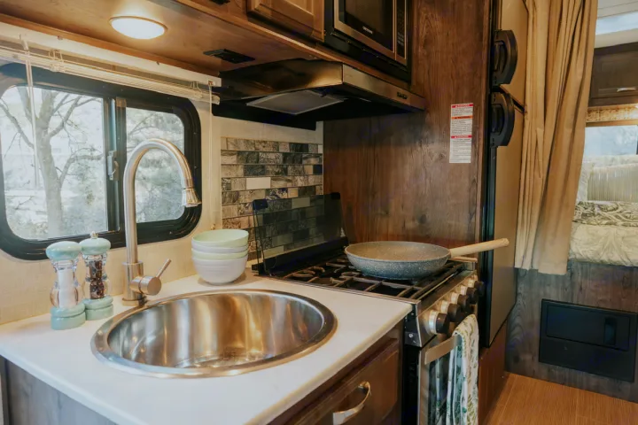 RV rental kitchen: modern, well-lit space with stainless steel sink, gas stove, microwave, and tiled backsplash.. Gulf Stream Conquest 2023
