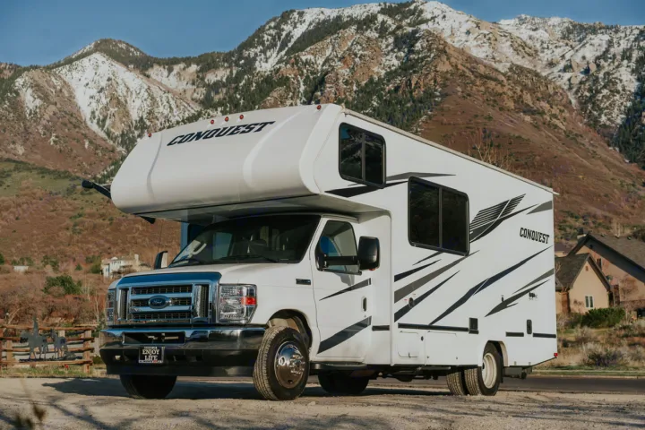 White Conquest motorhome RV rental, parked with snow-capped mountains in background. Perfect for travel.. Gulf Stream Conquest 2023