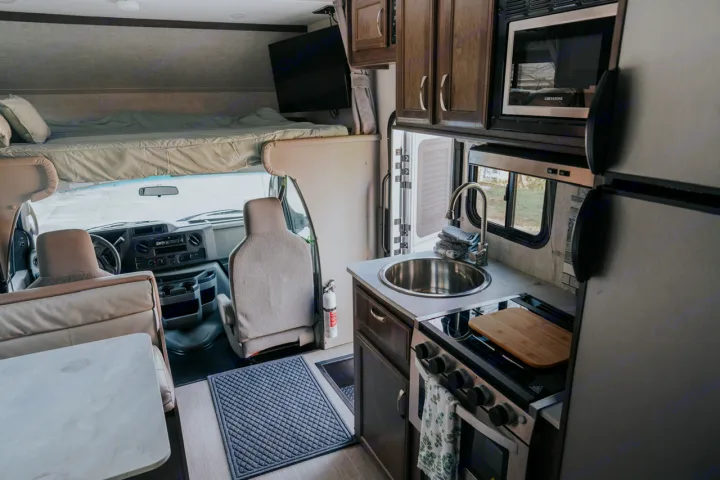 An rv rental interior featuring a compact kitchen with sink and stove, an overhead bed, and driver's cab. Ready for adventure.. Gulf Stream Conquest 2023