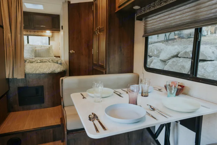 RV rental interior with a cozy dining booth and set table, plus a comfortable bed area.. Gulf Stream Conquest 2023