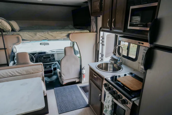 Step inside this RV rental! View of the spacious interior with an overhead bed, driver's area, dining table, and full kitchen.. Gulf Stream Conquest 2023