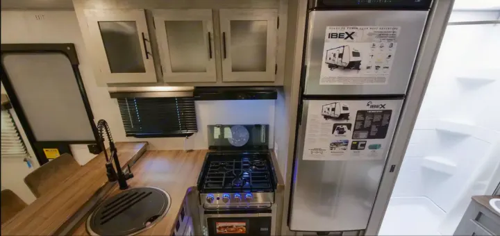 Explore this RV rental's interior: a compact kitchen with stove, sink, fridge, and an adjacent shower stall.. Forest River IBEXMBS 2023