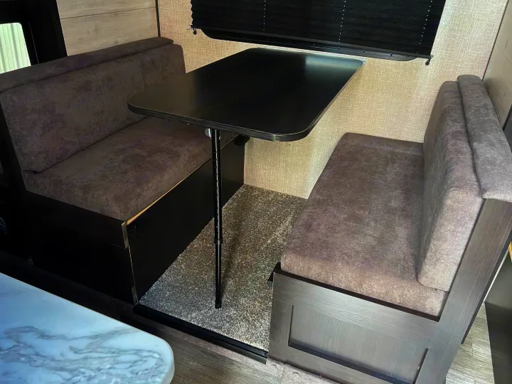 Comfortable RV rental dinette featuring grey upholstered booth seating, a dark wood-look table, and a plush rug.. Jayco Jay Flight SLX 2023
