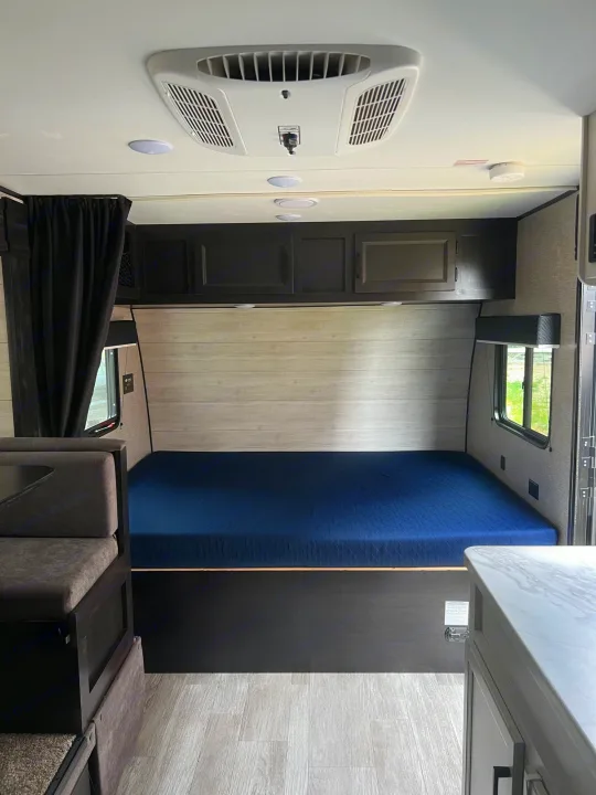 Inside a modern RV rental: blue bed, dinette, overhead cabinets, and AC unit. Ready for your adventure.. Jayco Jay Flight SLX 2023