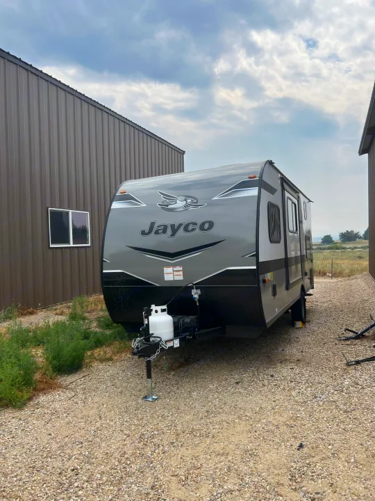 Gray Jayco travel trailer RV rental parked on gravel between buildings under a cloudy sky. Ready for your next journey.. Jayco Jay Flight SLX 2023