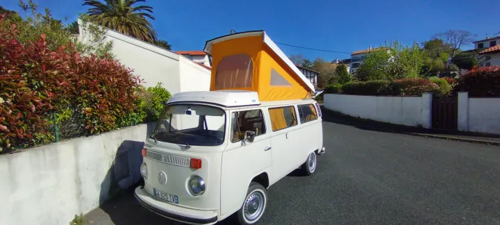 Vintage white VW pop-top camper van, ideal for RV rental. Parked on a sunny street with lush greenery.. Volkswagen T2 1978