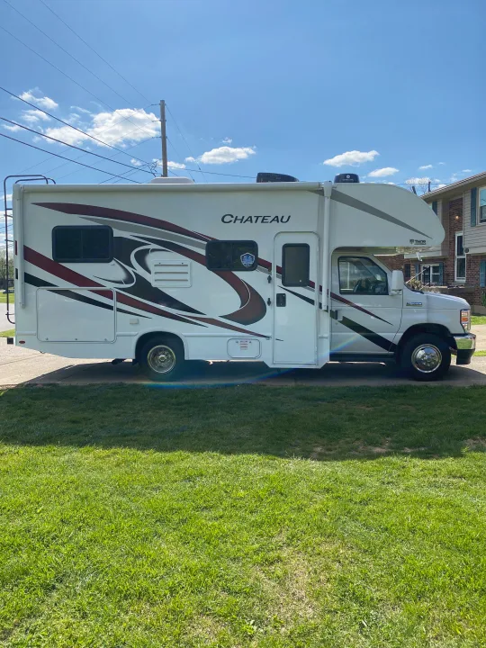 This white Chateau Class C RV rental is parked on a driveway beside green grass under a clear blue sky, ready for your adventure.. Ford F350 22E MC 2023
