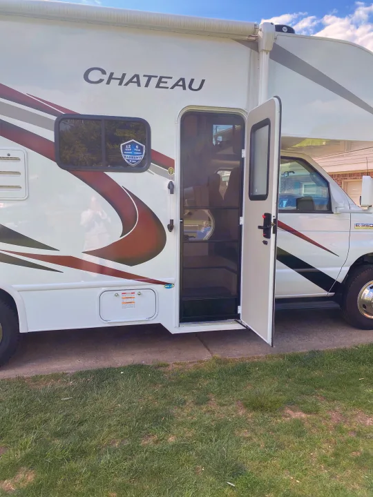 White Chateau RV rental parked with main door open, revealing screen. Thor warranty & E-350 Super Duty details are visible on side.. Ford F350 22E MC 2023