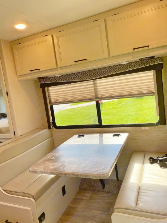 RV rental dinette: booth seating, table, and window with sunny grass views, ideal for meals or relaxing.. Ford F350 22E MC 2023