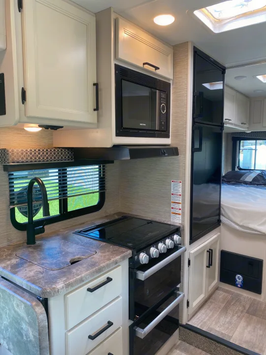 Well-appointed RV rental kitchen featuring a microwave, oven, sink, and refrigerator with light cabinetry.. Ford F350 22E MC 2023