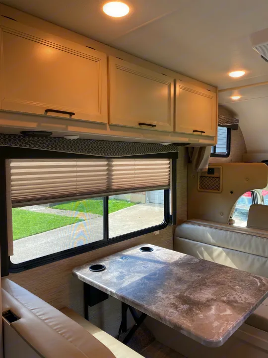 Interior of an RV rental showing a dinette with overhead cabinets, table, and seating by a window.. Ford F350 22E MC 2023