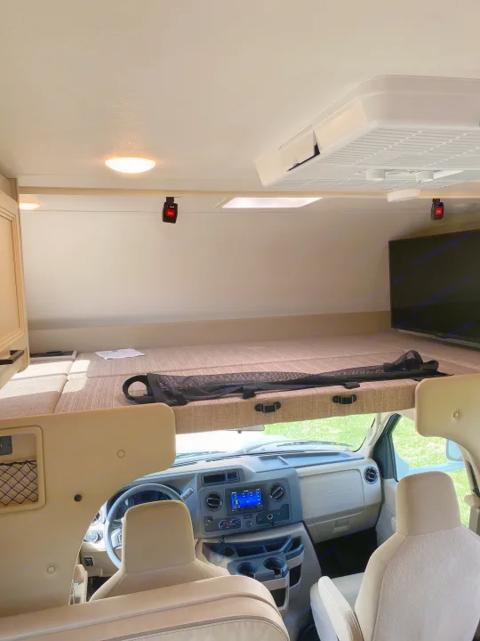 Interior of an **rv rental**, showcasing the overhead bunk, driver's cabin with dashboard, and front seats. AC unit is on the ceiling.. Ford F350 22E MC 2023