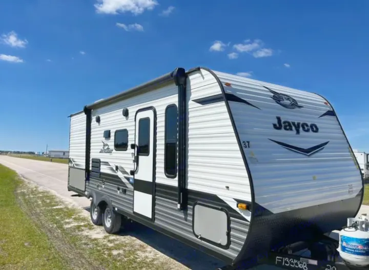Side view of a white and gray Jayco travel trailer RV rental with propane tanks, parked outdoors under blue sky.. Jayco Jay Flight SLX 2022