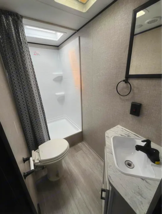 Modern RV rental bathroom with a compact shower, toilet, and sink vanity. Features a skylight and light-colored interior.. Jayco Jay Flight SLX 2022