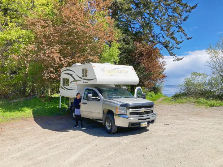 Woman by a silver pickup truck with an Adventurer truck camper. An ideal RV rental for scenic outdoor adventures.. Chevrolet Other 2010