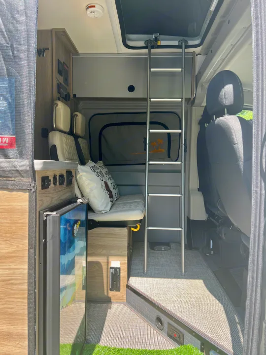 View inside a modern RV rental featuring a bunk bed, bench seating, compact fridge, and control panel for road trip comfort.. Winnebago Solis 2024