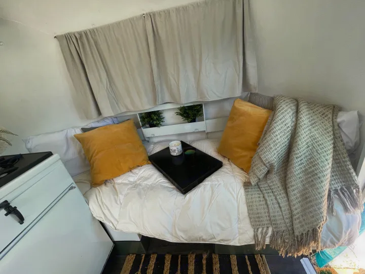 Cozy RV rental interior with a comfy bed, yellow pillows, a plant shelf, and a small white appliance.. Boler Holitrai 1976