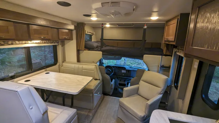 Spacious RV rental interior featuring a dinette, overhead bed, cabinets, cockpit view, and comfy lounge chair.. Adventurer Ford Transit 2020