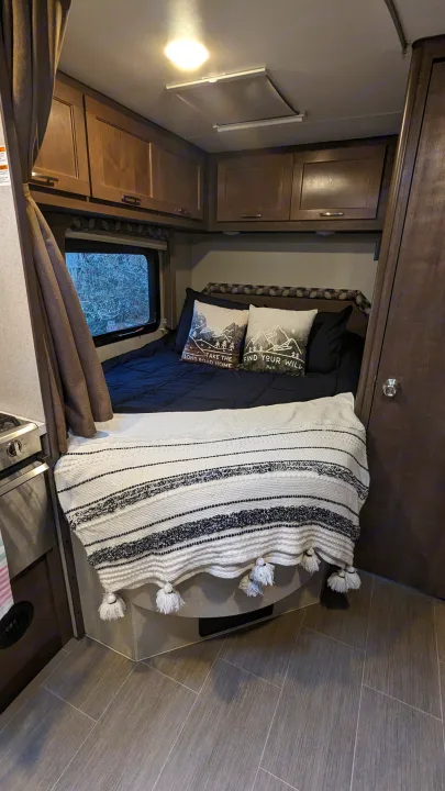 Cozy RV rental interior: bedroom with nature-themed pillows, kitchenette, and wood cabinets. Perfect for travel adventures.. Adventurer Ford Transit 2020