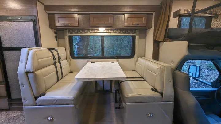 RV rental's cozy interior: dinette with table & seating, kitchen area with fridge, and overhead bunk.. Adventurer Ford Transit 2020
