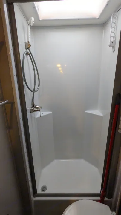 A clean, compact shower in an RV rental, featuring a handheld sprayer, corner seats, a ceiling light, and drying rack.. Adventurer Ford Transit 2020