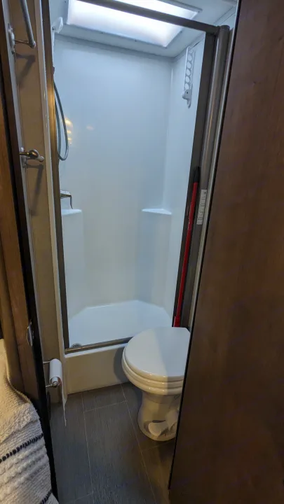 Inside a compact RV rental bathroom: a clean white shower, toilet, and modern gray flooring for comfortable travels.. Adventurer Ford Transit 2020