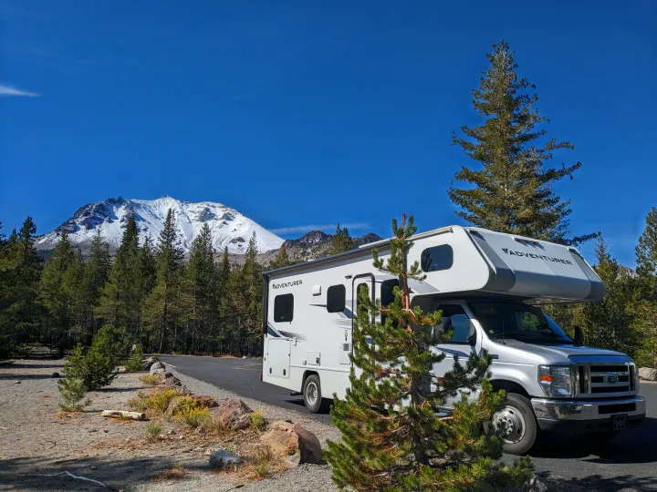 An Adventurer RV rental parked with a stunning view of a snow-capped mountain, surrounded by pine forests under a clear blue sky.. Adventurer Ford Transit 2020